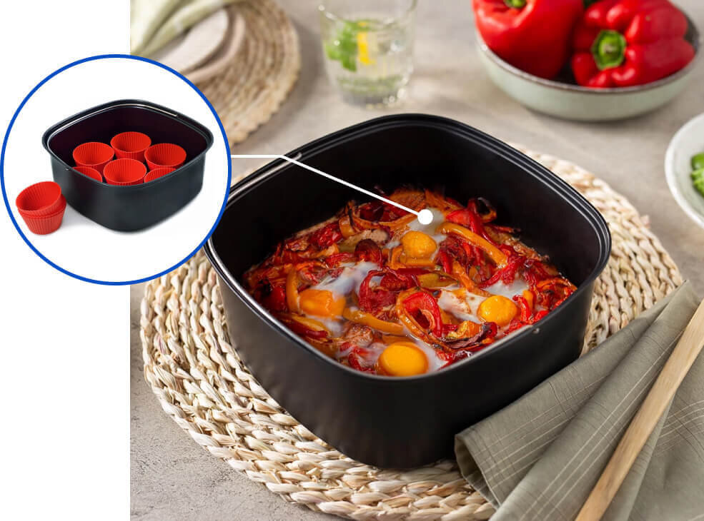 Na obrazie widoczna jest czarna miska z potrawą z jajkami i warzywami, umieszczona na plecionym podkładzie. W okrągłym wstawce pokazano tę samą miskę z czerwonymi silikonowymi foremkami w środku.