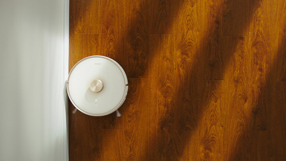 Robot sprzątający na drewnianej podłodze, widoczny z góry. Na urządzeniu znajduje się logo \'Lenovo\'.