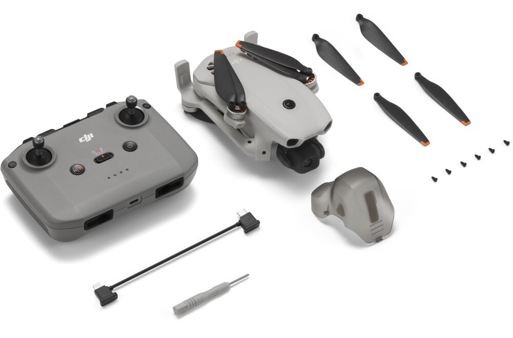 Dron DJI Lito 1 Na białym tle rozłożone są elementy zestawu drona: szary dron ze złożonymi śmigłami, cztery zapasowe czarne śmigła, szary pilot zdalnego sterowania, śrubokręt, zapasowe śruby, kabel USB, instrukcja obsługi i osłona gimbala