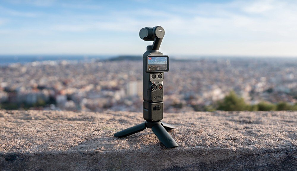 Kamera sportowa DJI OSMO POCKET 4 urządzenie z kamerą ustawione na trójnogu na kamiennym murku, w tle widać panoramę miasta