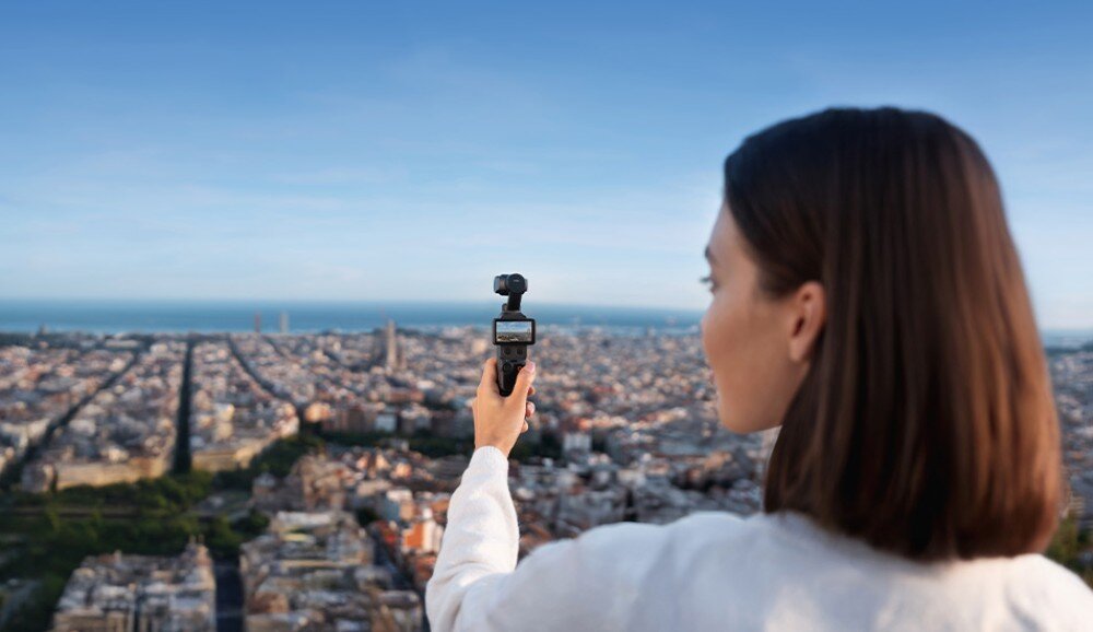 Kamera sportowa DJI OSMO POCKET 4 osoba widziana od tyłu trzymająca urządzenie z kamerą skierowane na panoramę miasta rozciągającą się przed nią