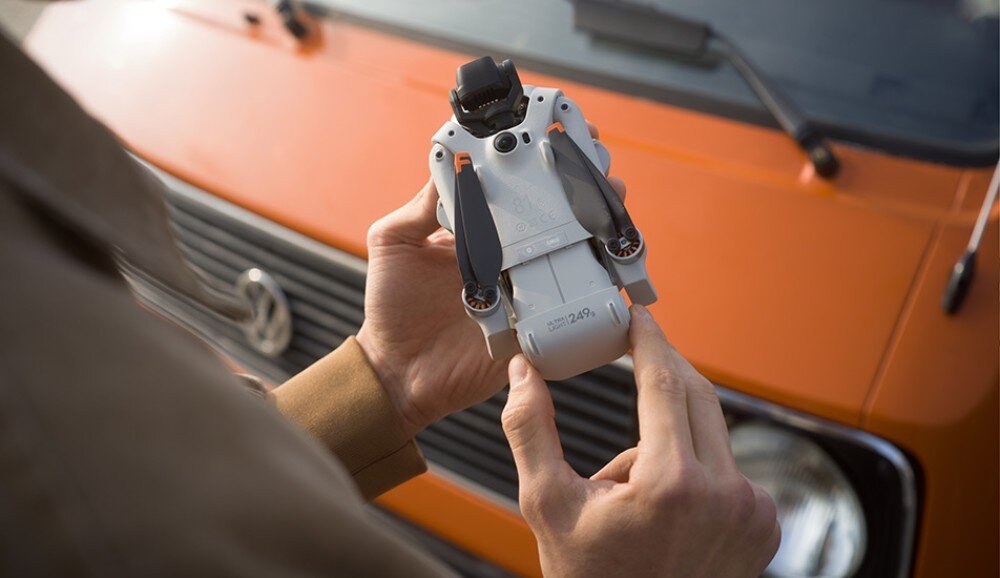Dron DJI Lito X1 zbliżenie na dłonie trzymające złożonego drona z napisem ULTRA LIGHT 249g na obudowie na tle maski pomarańczowego auta
