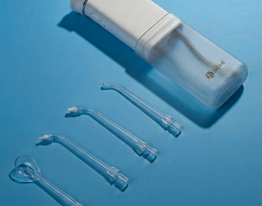 Irygator do zębów HAXE HX714 Dokładne czyszczenie resztki jedzenia i osad wspiera zdrowie dziąseł i redukuje ryzyko stanów zapalnych 1450 impulsów na minutę z przestrzeni międzyzębowych na zdjęciu irygator lezy obok końcówki niebieskie tło