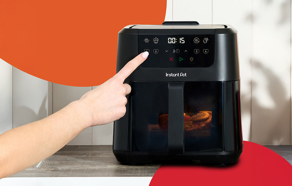 Czarna frytkownica beztłuszczowa Instant Pot Vortex Compact 5L z panelem dotykowym, na którym widoczny jest czas 00:15. Osoba dotyka jednego z przycisków na panelu, a wewnątrz urządzenia widać jedzenie.