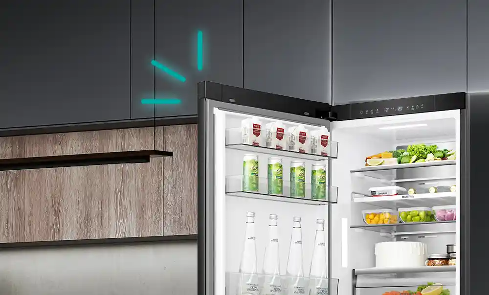 Otwarta lodówka z widocznymi półkami wypełnionymi produktami spożywczymi, takimi jak napoje, warzywa i pojemniki z jedzeniem. Na górnej krawędzi drzwi znajduje się panel sterowania z ikonami i wyświetlaczem.