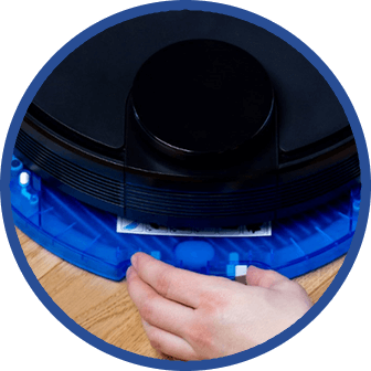Osoba wkłada filtr do niebieskiego odkurzacza automatycznego. Urządzenie znajduje się na drewnianej podłodze.