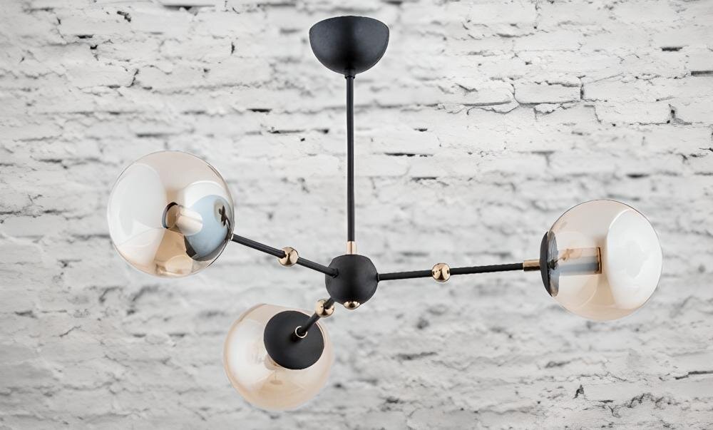 Lampa sufitowa z trzema kulistymi kloszami w kolorze czarnym, zamontowana na tle białej ceglanej ściany. Klosze są przymocowane do centralnego punktu za pomocą metalowych ramion.