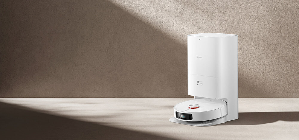 Na obrazie widoczny jest biały robot sprzątający z okrągłą podstawą i stacją dokującą. Na stacji znajduje się logo \'XIAOMI\'.