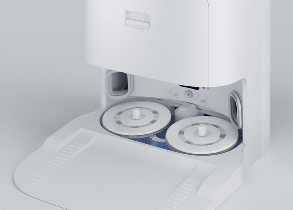 Obraz przedstawia otwartą komorę robota sprzątającego z widocznymi dwoma okrągłymi elementami wewnętrznymi. Obudowa jest w kolorze białym.