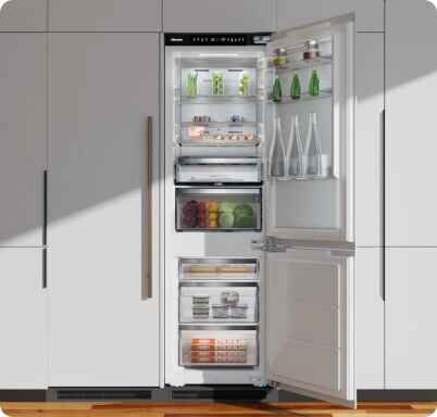 Otwarta lodówka z widocznymi półkami, na których znajdują się butelki, słoiki i pojemniki z jedzeniem. Wnętrze jest dobrze oświetlone, a drzwi lodówki mają dodatkowe półki na mniejsze produkty.