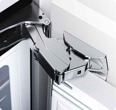 Zbliżenie na metalowy zawias drzwi lodówki, ukazujący jego konstrukcję i sposób montażu. Elementy są wykonane z błyszczącego metalu.