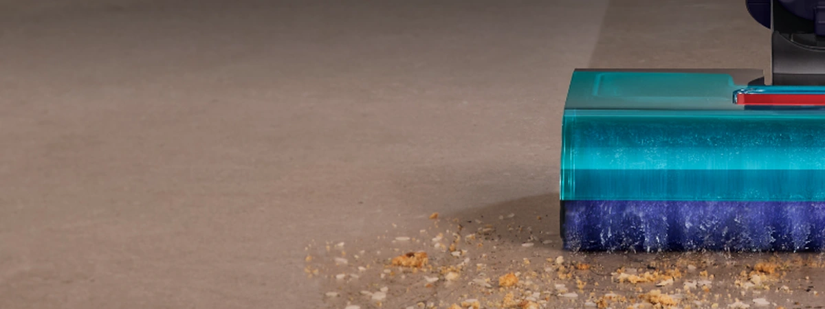 Zbliżenie na lewą stronę szczotki mopa podczas pracy. Wałek zbiera zabrudzenia, okruchy i myje plamy na podłodze