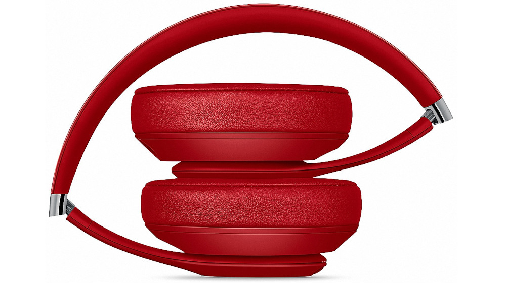 Na obrazie widoczne są czerwone słuchawki nauszne z metalicznymi elementami przy zawiasach. Słuchawki są złożone, a ich nauszniki i pałąk mają teksturowaną powierzchnię.