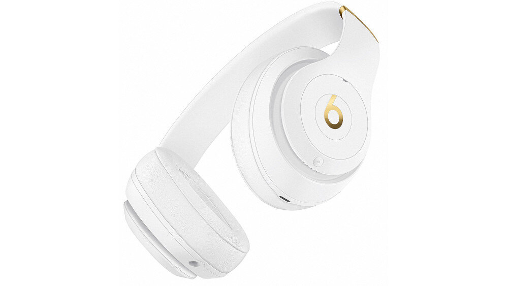 Białe słuchawki nauszne z widocznym złotym logo \'b\' na nauszniku. Słuchawki mają elegancki, nowoczesny design.