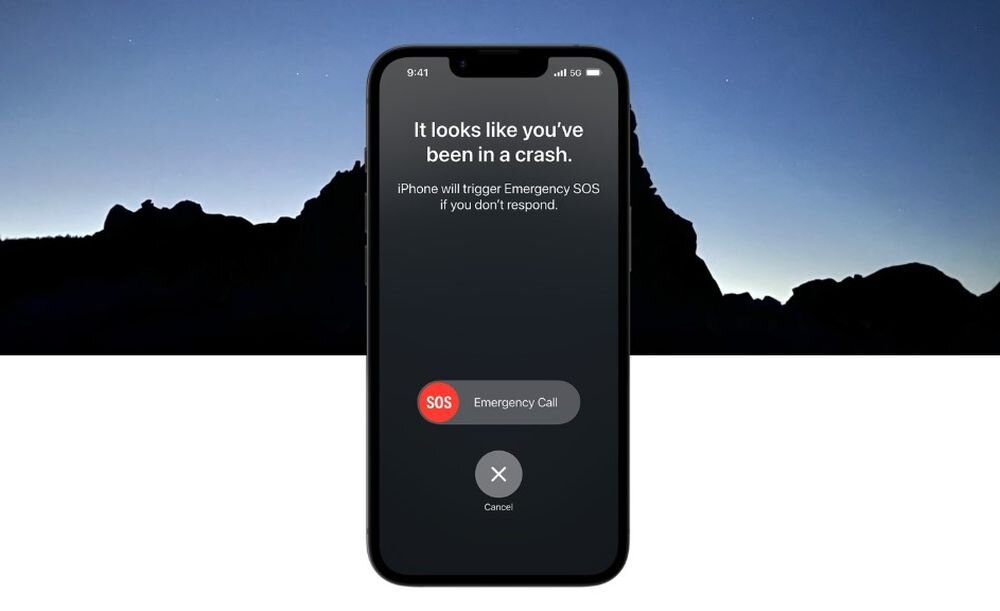 Na ekranie smartfona widoczny jest komunikat: \'It looks like you\'ve been in a crash. iPhone will trigger Emergency SOS if you don\'t respond.\' Poniżej znajdują się przyciski \'SOS Emergency Call\' oraz \'Cancel\'.