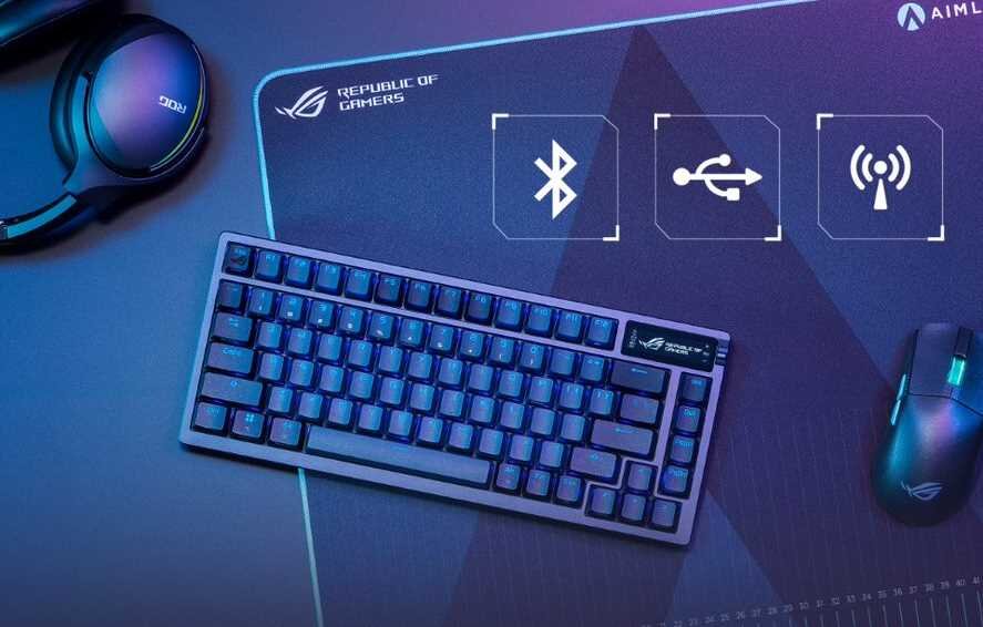 Na obrazie znajduje się klawiatura mechaniczna z podświetleniem RGB, mysz komputerowa oraz słuchawki na dużej podkładce z logo \'Republic of Gamers\'. Widoczne są ikony Bluetooth, USB i sygnału bezprzewodowego.