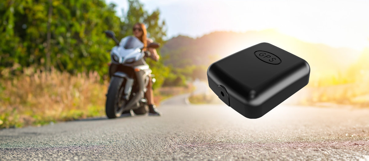Na obrazie widoczny jest czarny, kompaktowy urządzenie z napisem \'GPS\' na górze, umieszczone na tle rozmytego krajobrazu z motocyklem i osobą w oddali.