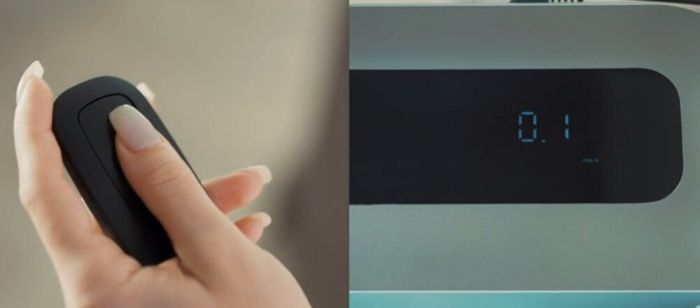 Po lewej stronie widoczna jest dłoń trzymająca czarny pilot z przyciskiem. Po prawej stronie znajduje się wyświetlacz z cyfrą \'0.1\'.