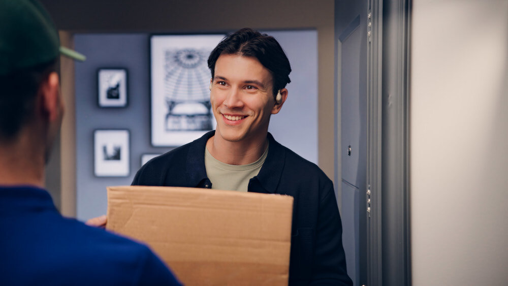 Słuchawki powietrzne PANASONIC RB-F10 - Szybki zastrzyk energii, do 7 godzin na jednym ładowaniu, z etui do 25 godzin na jednym ładowaniu, osoba z założonymi słuchawkami powietrznymi odbierająca paczkę