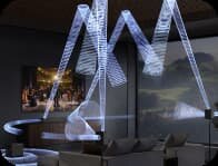 W pomieszczeniu znajduje się zestaw kina domowego z widocznymi efektami świetlnymi symbolizującymi dźwięk przestrzenny. Na ścianie wisi obraz przedstawiający scenę teatralną.