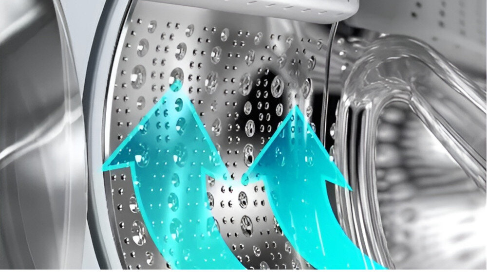 Obraz przedstawia wnętrze bębna pralki z widocznymi otworami na powierzchni. Na bębnie znajdują się dwie niebieskie strzałki skierowane ku górze, symbolizujące przepływ wody lub powietrza.
