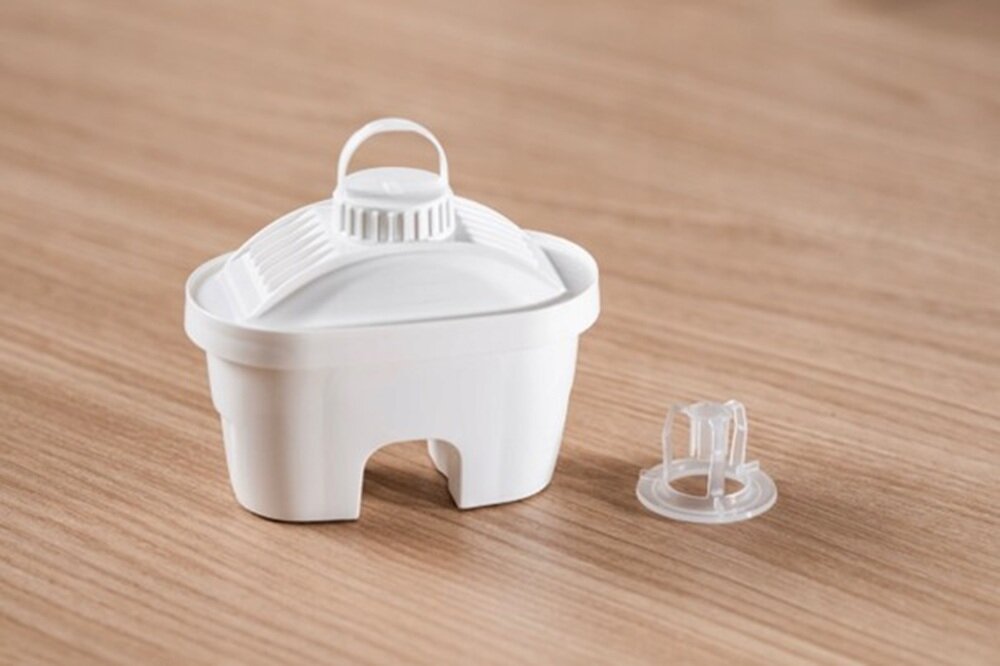 Na drewnianym blacie znajduje się biały wkład filtrujący o zaokrąglonym kształcie oraz przezroczysty element plastikowy obok niego.