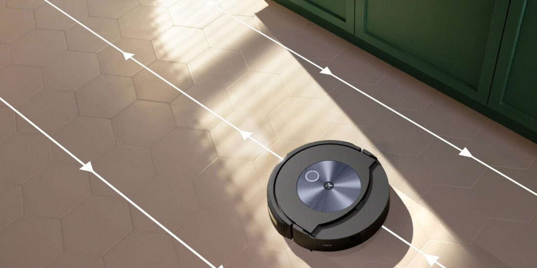Robot sprzątający na podłodze z sześciokątnymi płytkami, z widocznymi liniami kierunkowymi. W tle znajduje się szafka w ciemnym kolorze.
