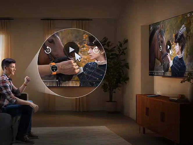 Osoba siedzi na kanapie i ogląda telewizor, na którym wyświetlany jest film z kobietą i koniem. Obok telewizora znajduje się drewniana szafka, a na ekranie widoczny jest symbol odtwarzania wideo.