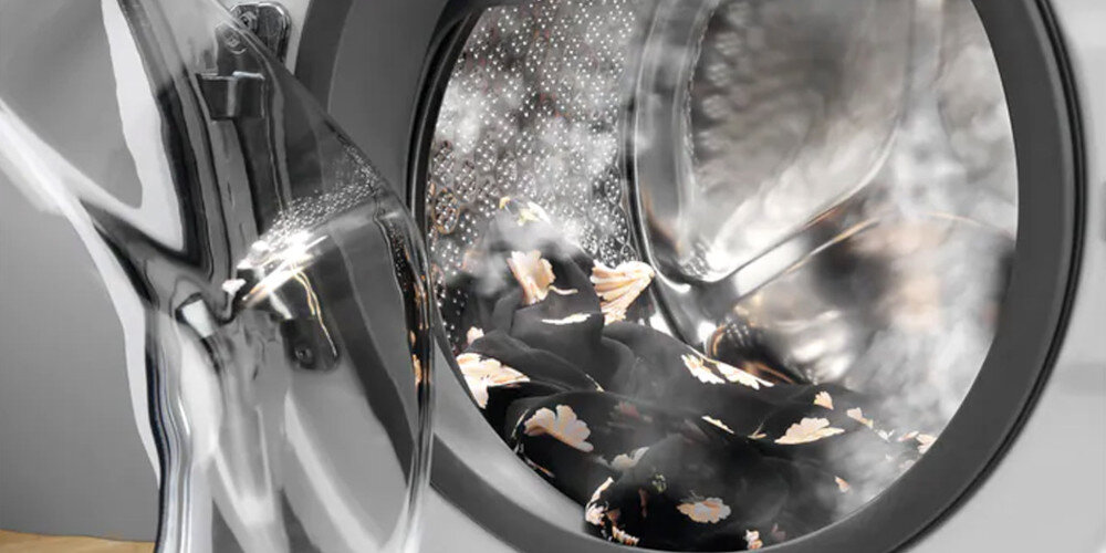 Obraz przedstawia wnętrze bębna pralki z widoczną parą i ubraniami w środku. Pralka jest w trakcie cyklu prania parowego.