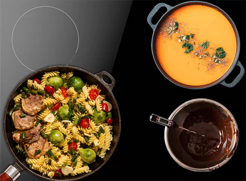 Na płycie kuchennej znajdują się trzy naczynia: patelnia z makaronem, brukselką i mięsem, garnek z pomarańczową zupą oraz rondel z ciemnym sosem i termometrem. Płyta ma widoczny okrągły obrys pola grzewczego.