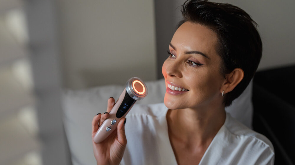 Osoba trzyma urządzenie do mezoterapii bezigłowej z podświetlonym okręgiem na końcu. Urządzenie ma ciemny panel z przyciskami.