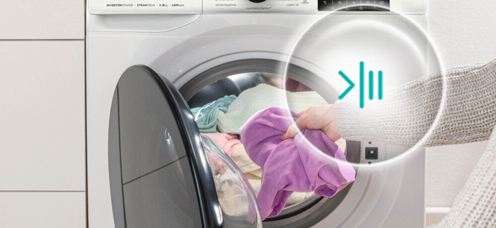 Osoba wkłada kolorowe ubrania do otwartej pralki. Na obrazie widoczny jest symbol \'>\' oraz dwie pionowe linie, przypominające przycisk pauzy.