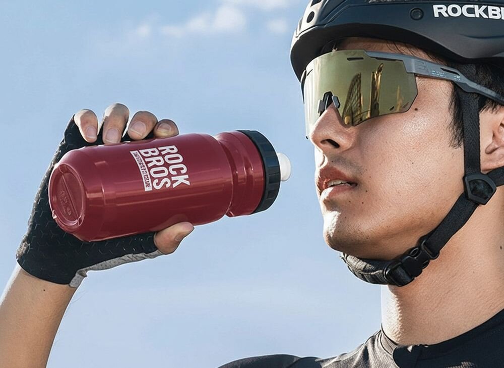 Bidon ROCKBROS 35210066003 600 ml Czerwony, picie, woda, sport, trasa, Bidon leżący obok rakiety tenisowej.