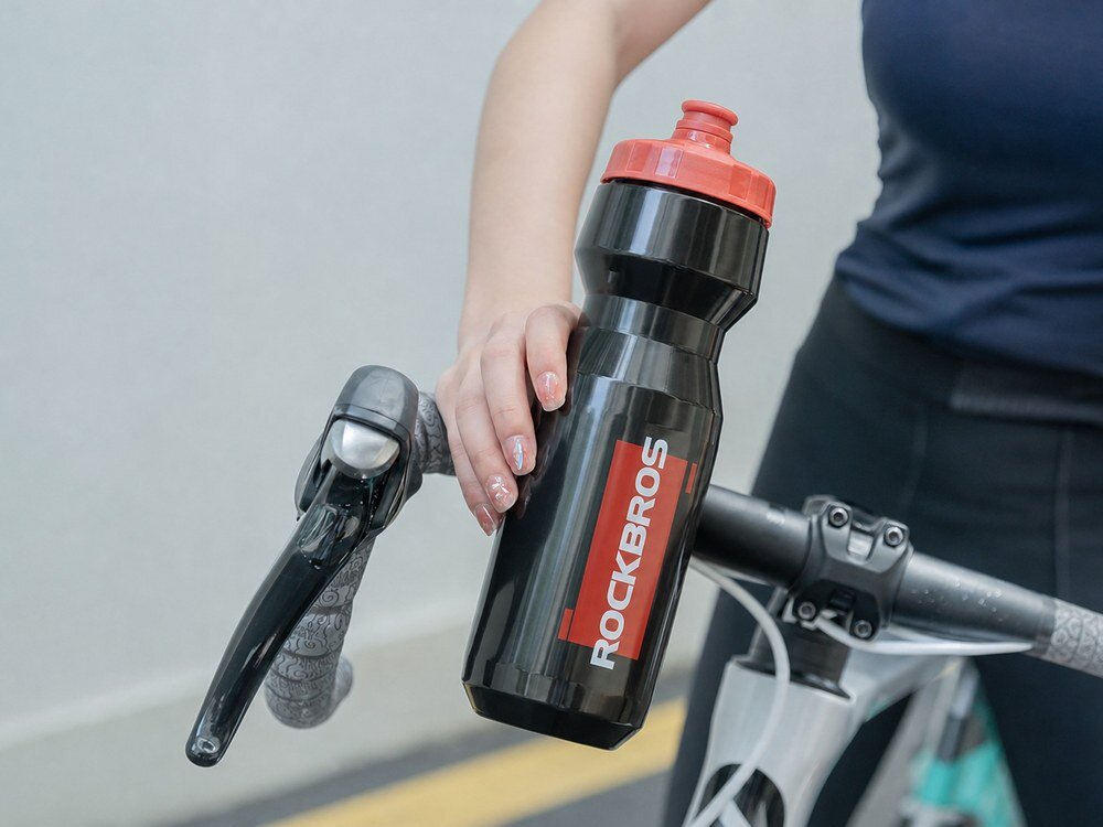 Bidon ROCKBROS DCBT69BR 750 ml Czarno-czerwony, woda, sport, rower, picie, Ręka z butelką przy kierownicy roweru.