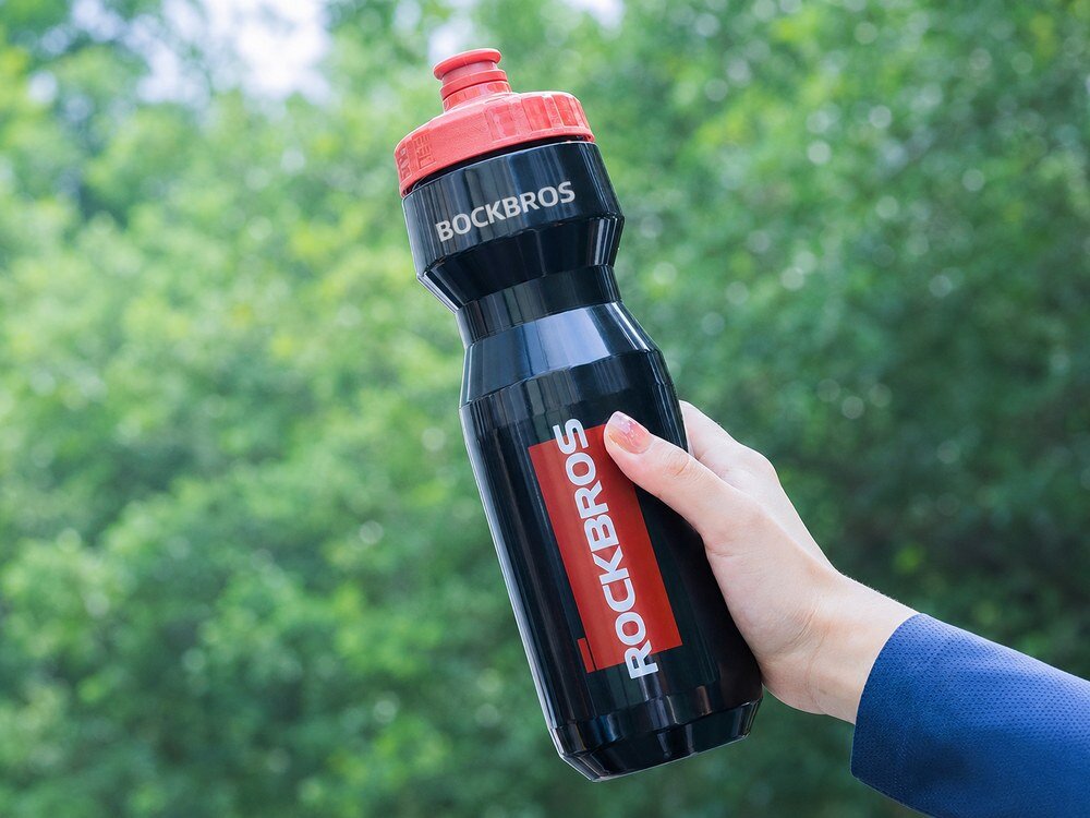 Bidon ROCKBROS DCBT69BR 750 ml Czarno-czerwony, trasa, trening, napój, nawodnienie, Ręka trzymająca bidon na tle zieleni.