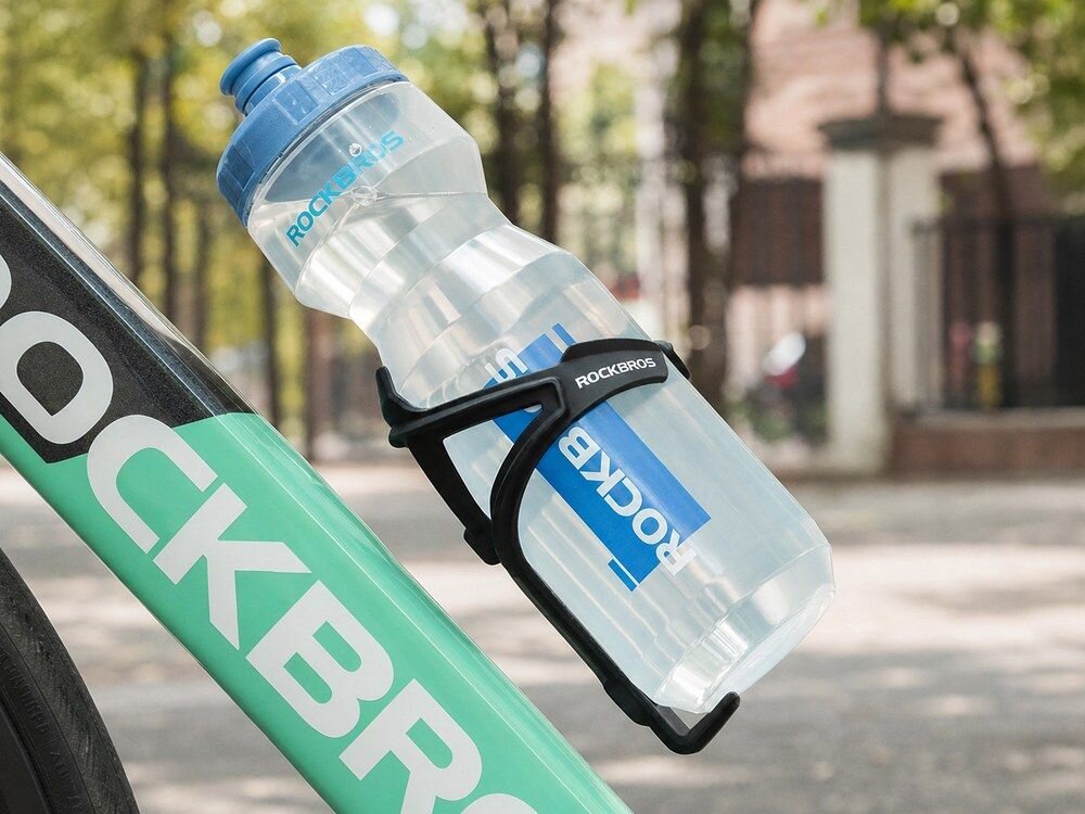 Bidon ROCKBROS DCBT69TB 750 ml Przezroczysto-niebieski, polipropylen, wytrzymałość, korek, smak, Butelka obok hantla, telefonu i zegarka.