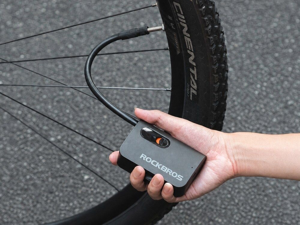 Pompka rowerowa elektryczna ROCKBROS L1 Mini, powietrze, pompowanie, rower, ciśnienie, Dłoń trzymająca pompkę elektryczną pompuje koło roweru.