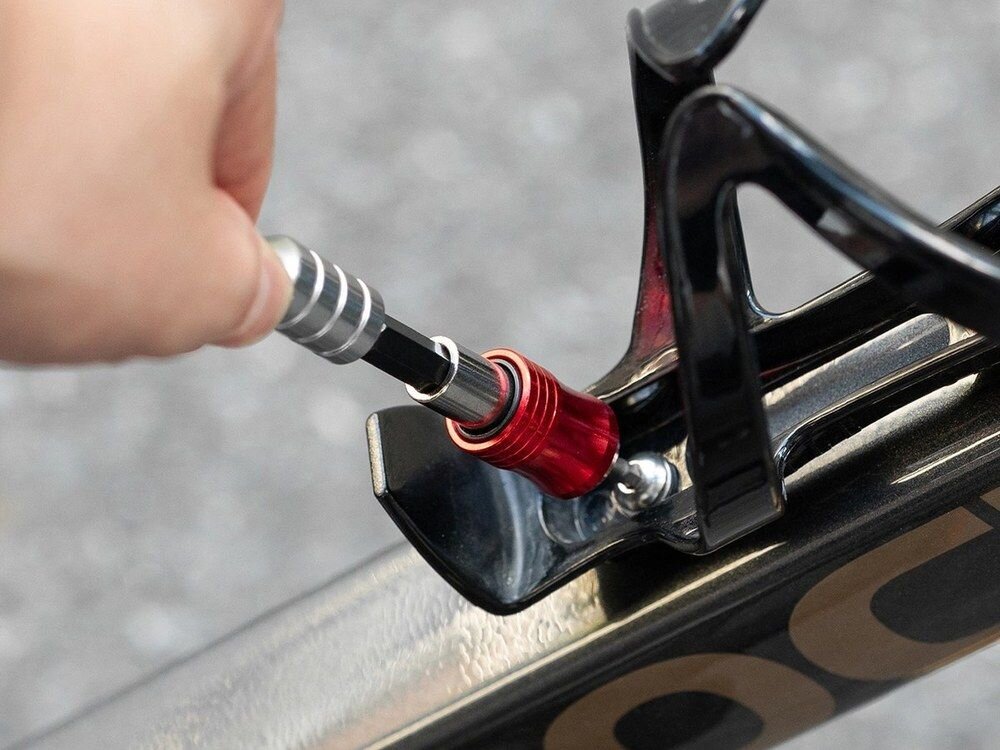 Osoba używa klucza rowerowego do regulacji elementu w rowerze. Klucz ma metaliczny uchwyt i czerwony element mocujący.