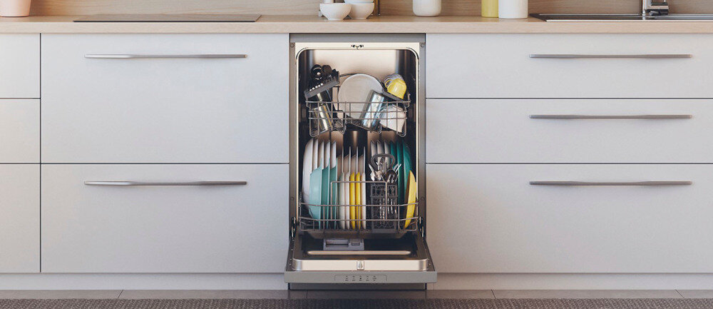 Zmywarka w zabudowie kuchennej z otwartymi drzwiami, wypełniona naczyniami, w tym talerzami i szklankami. Fronty szafek są białe z metalowymi uchwytami.