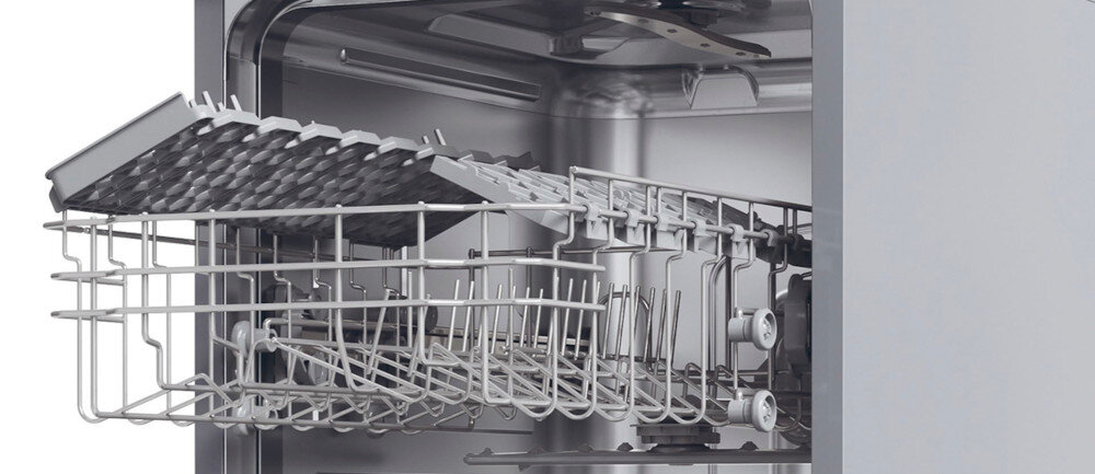 Wnętrze zmywarki z widocznym górnym koszem na naczynia i metalowymi elementami konstrukcyjnymi. Kosz jest częściowo wysunięty, a w tle widać stalowe ściany urządzenia.