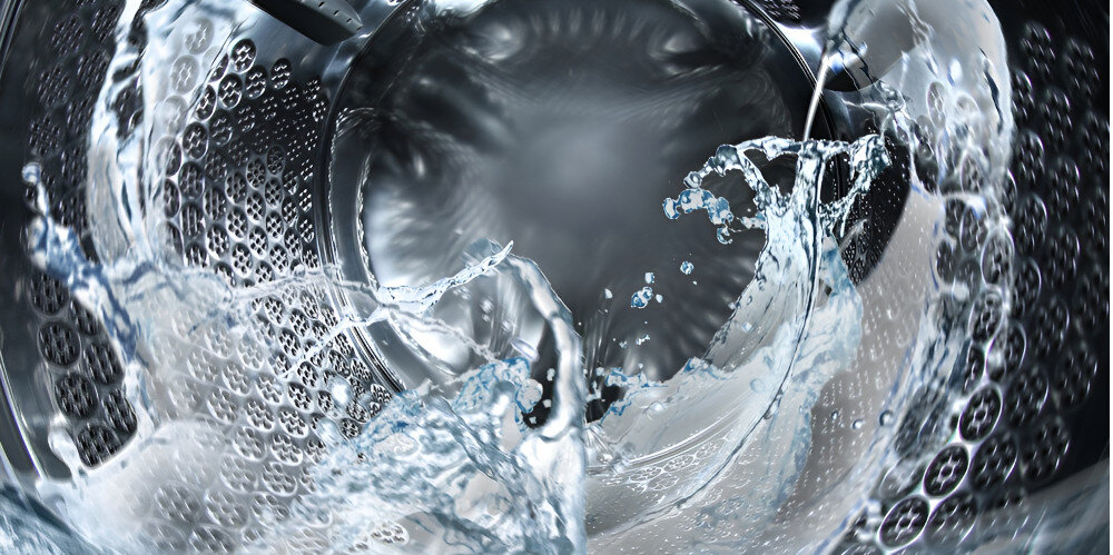 Obraz przedstawia wnętrze bębna pralki z wirującą wodą. Widać dynamiczny ruch wody i metalową powierzchnię bębna.