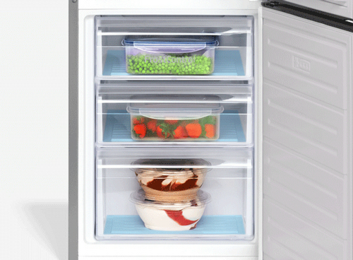 Otwarta zamrażarka z trzema przezroczystymi szufladami, w których znajdują się pojemniki z mrożonymi produktami: groszkiem, truskawkami i deserem. Wnętrze jest jasne, a szuflady mają niebieskie podkładki.