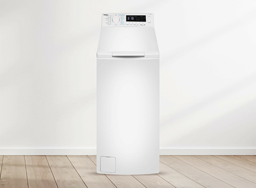 Biała pralka ładowana od góry stoi na drewnianej podłodze. Na panelu sterowania widoczny jest wyświetlacz i pokrętło z różnymi ustawieniami.