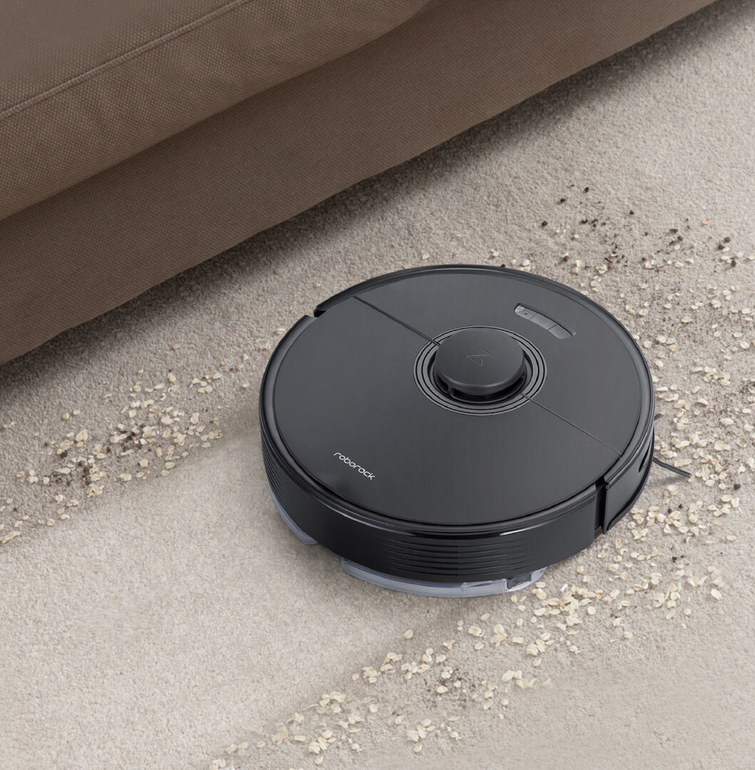 Czarny robot sprzątający na dywanie z rozsypanymi drobinkami. Widoczne logo: roborock.