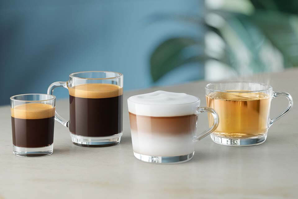 Na obrazie widoczne są cztery szklanki z różnymi napojami: espresso, kawa z pianką mleczną, kawa z mlekiem oraz herbata. Szklanki stoją na jasnym blacie, a w tle widać rozmyte zielone liście.