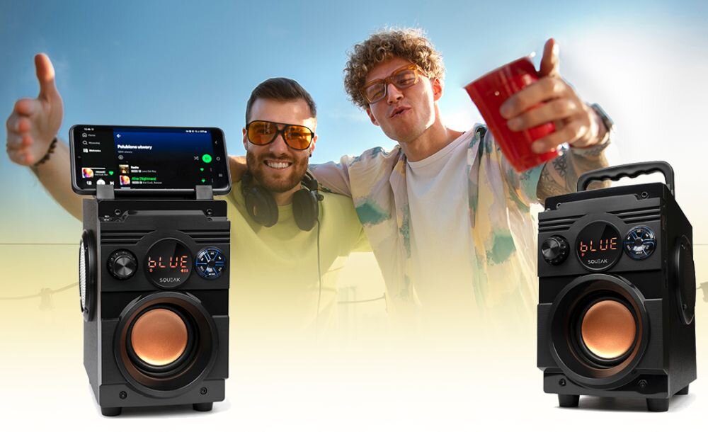 Na obrazie widoczne są dwa czarne głośniki mobilne z wyświetlaczem LED pokazującym napis \'BLUE\' oraz logo \'SQUEAK\'. W tle znajdują się dwie osoby w okularach przeciwsłonecznych, jedna z nich trzyma czerwony kubek.