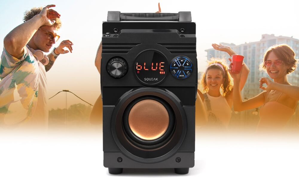 Czarny głośnik mobilny z wyświetlaczem pokazującym napis \'BLUE\' oraz dużym głośnikiem niskotonowym. W tle widoczni są ludzie w letnich strojach, trzymający czerwone kubki.