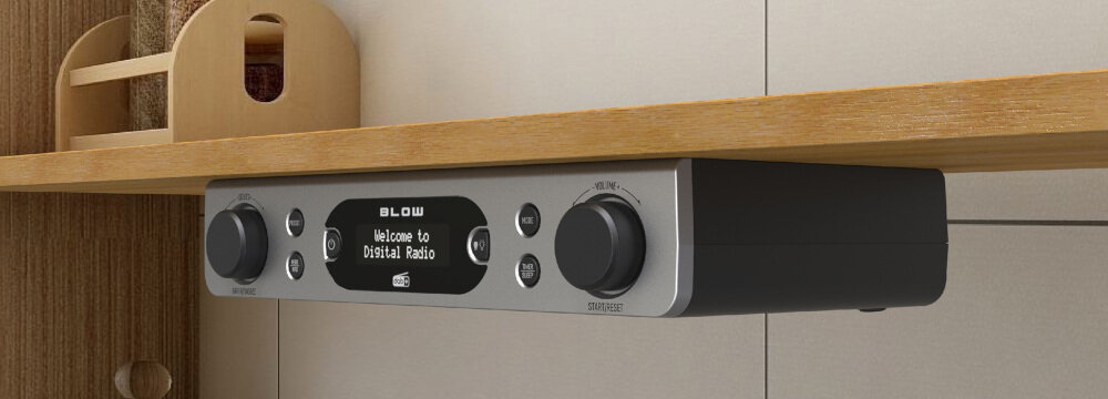 Podwieszane radio z wyświetlaczem pokazującym tekst \'Welcome to Digital Radio\'. Obudowa jest srebrna z czarnymi pokrętłami i logo \'BLOW\'.