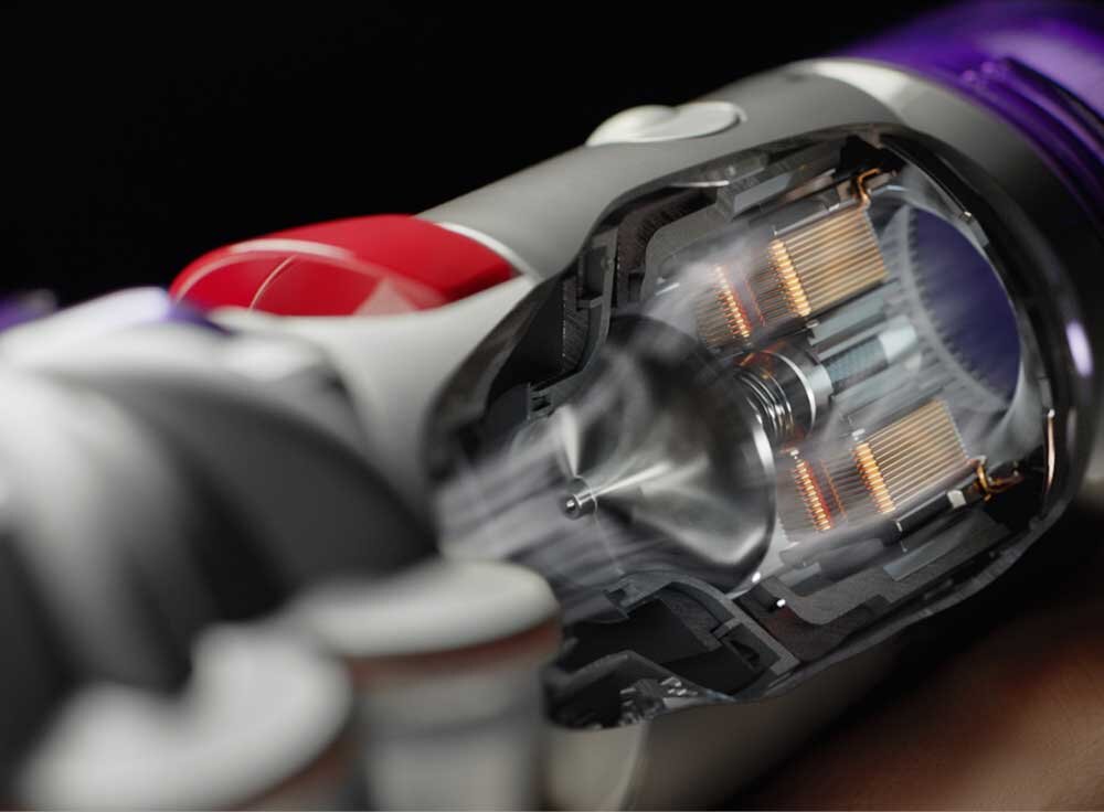 Zbliżenie na wnętrze odkurzacza z widocznymi elementami technicznymi, takimi jak cewki i wirnik. Obudowa jest w kolorach szarym, czerwonym i fioletowym.