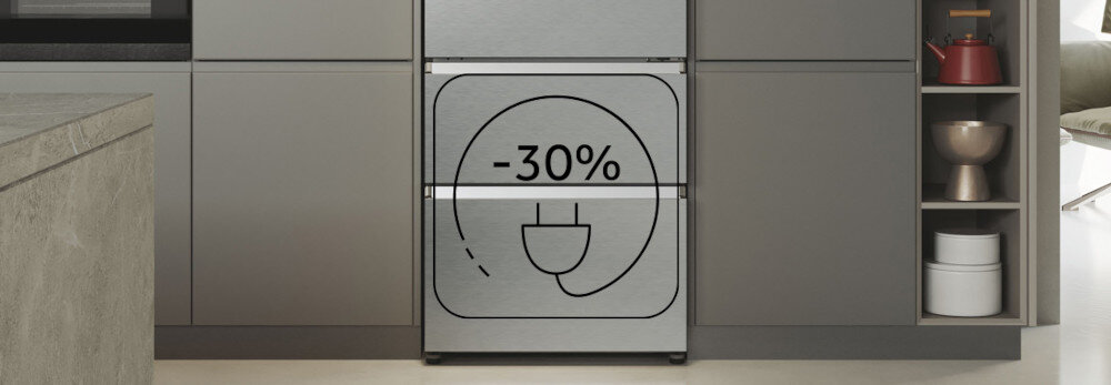 Lodówka w kolorze platynowy inox z napisem \'-30%\' i symbolem wtyczki na drzwiach. W tle widoczna jest nowoczesna kuchnia z szarymi szafkami.